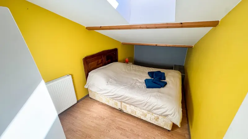 Une chambre aux murs jaunes sous les toits, avec un lit double