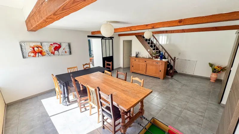 La salle à manger, sa grande table en bois et ses poutres apparentes