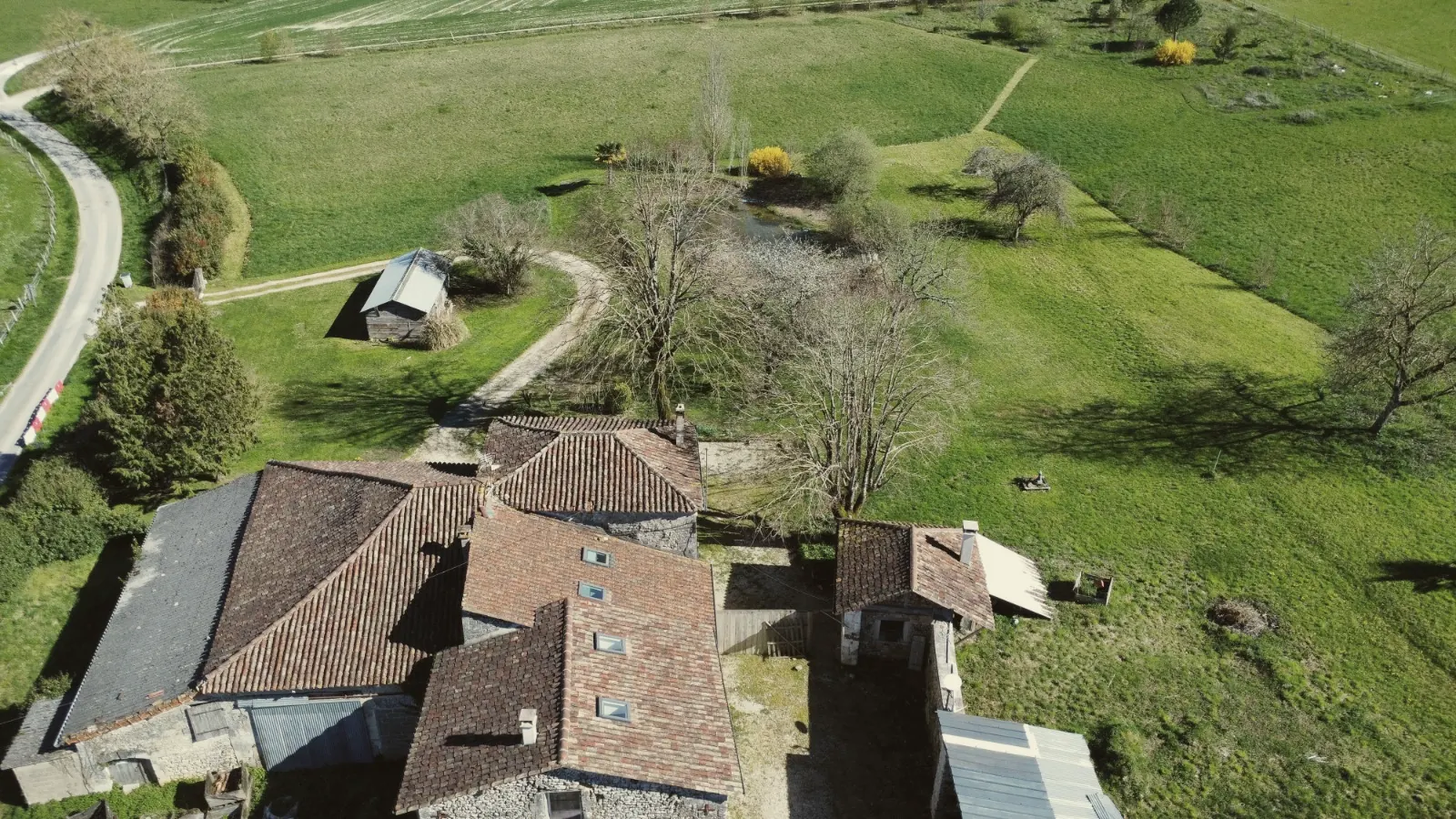 Vue aérienne du gîte : les toits de la ferme, le pré, l'étang et les arbres